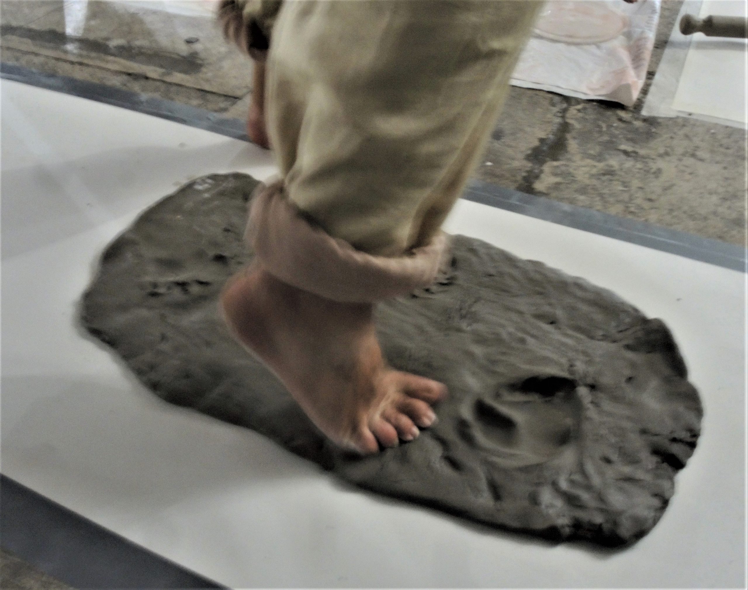 A participant dancer has their socks off, and their barefoot is pushing into a slab of grey clay
