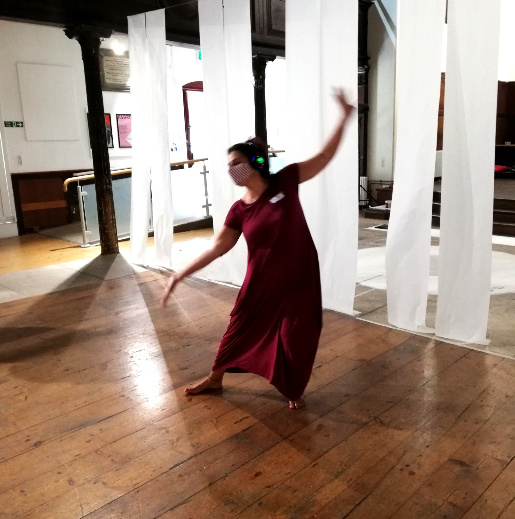 One of the project participants is improvising to sounds coming over her headphones. She is captured in a lovely pose -one arm is lifted high, the other is low, with her right foot out and the weight on her left bended leg. She is wearing on long red dress